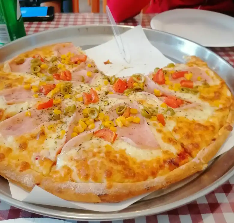 Pizza Rarytasu z szynką, papryką i kukurydzą na metalowej tacy, na stole w czerwono-białą kratkę