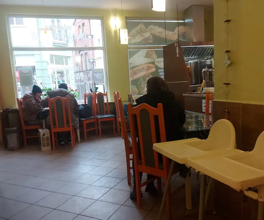 Sala baru: drewniane stoły i krzesła, jasne ściany i lada